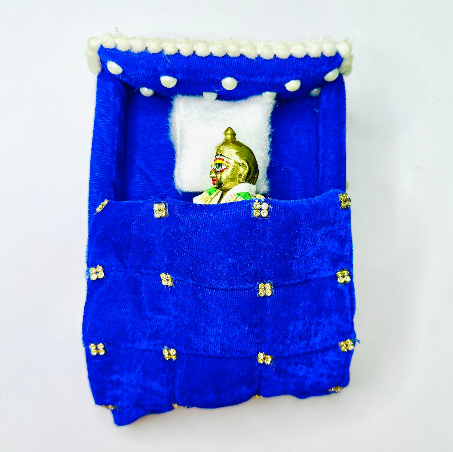 Top view of Laddu gopal ji sleeping in a Blue Shaneel Pearl Work Wooden Laddu Gopal Bed with Blanket & Pillow.