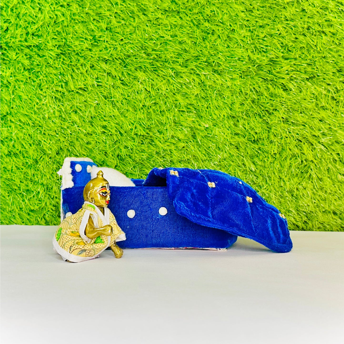 Kanha ji sitting beside a Blue Shaneel Pearl Work Wooden Laddu Gopal Bed with Blanket & Pillow.