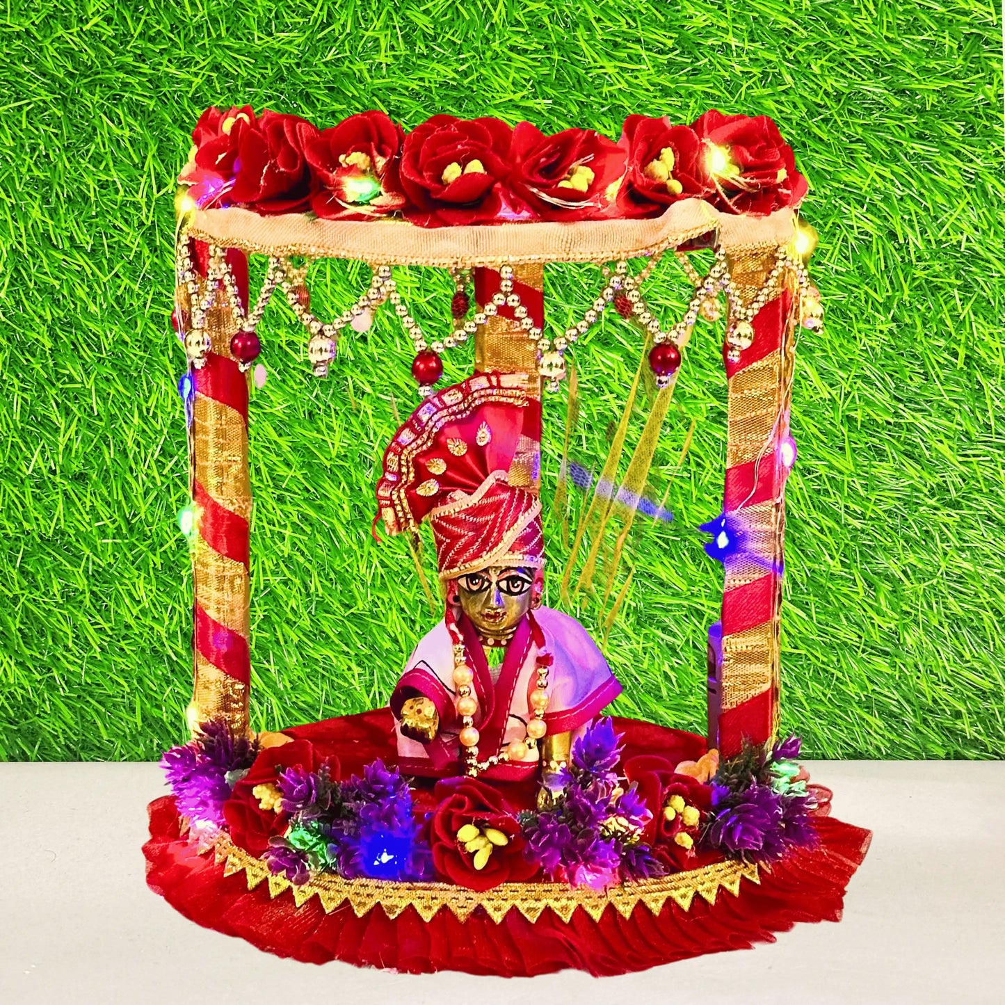 Laddu gopal ji sitting on a decorative Red Floral Laddu Gopal Singhasan Bed with Pearl Hangings & LED Lights.