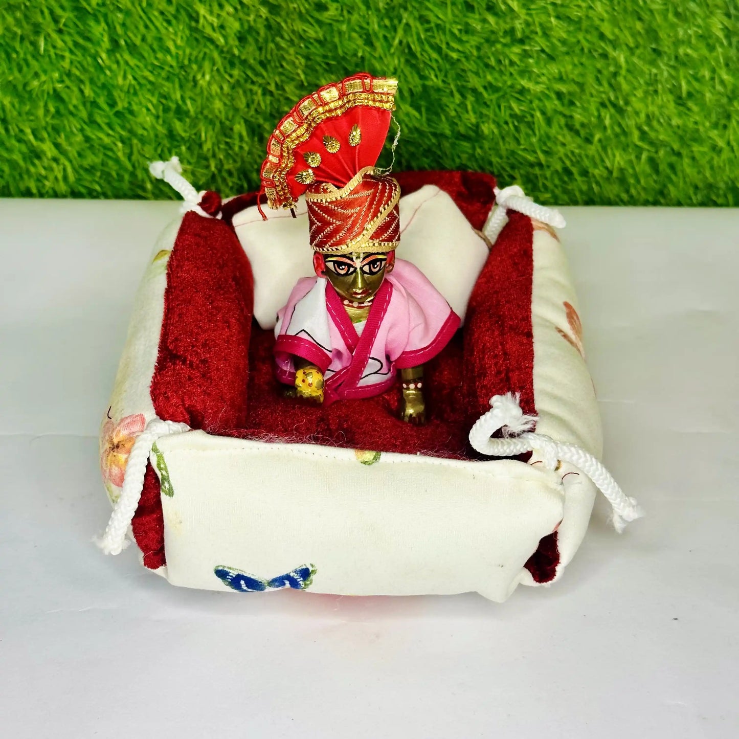 Top View of Laddu Gopal ji sitting in a Elegant Floral Print Laddu Gopal Bedding Set with Red Velvet Base & Blanket.