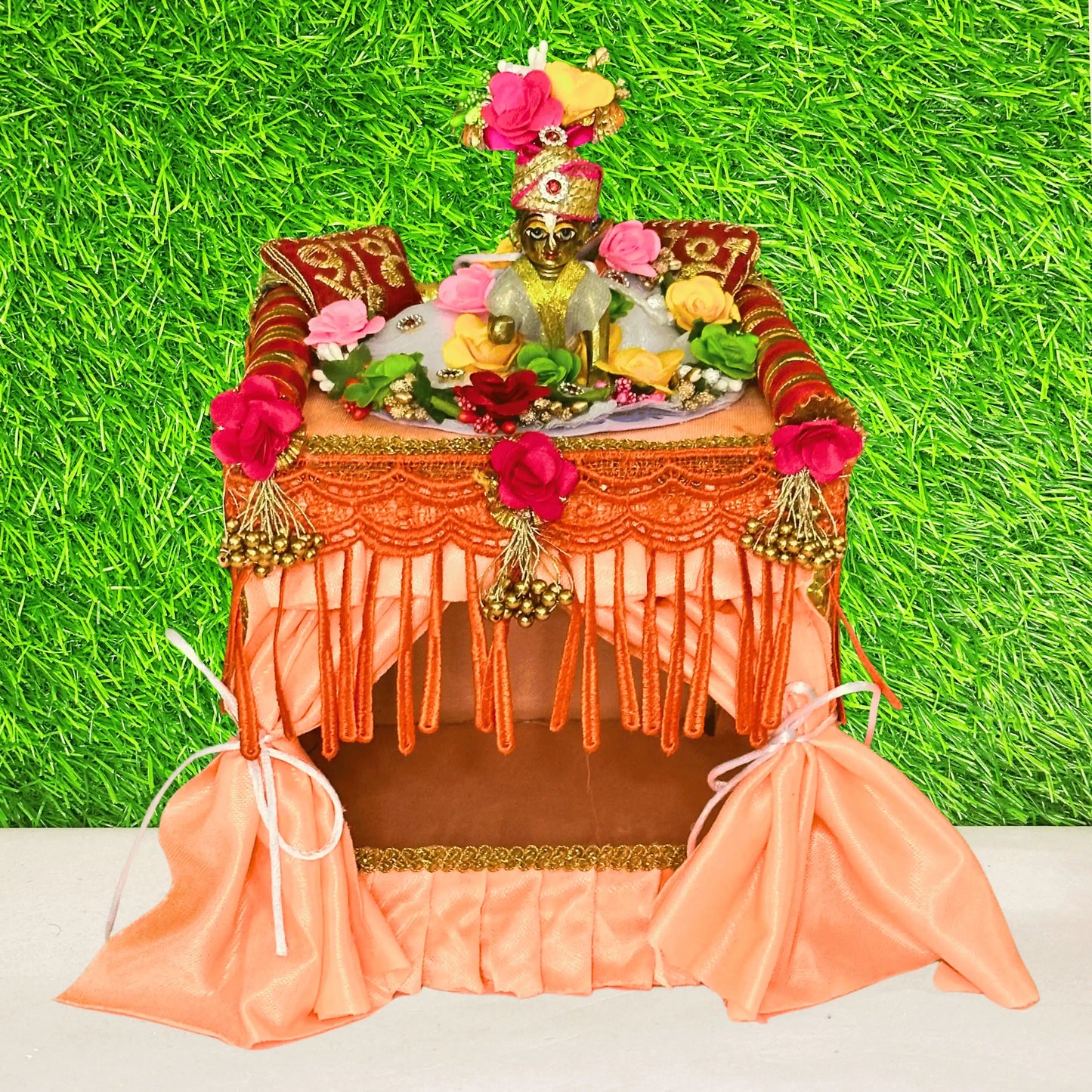 Laddu gopal ji sitting on a peach color Velvet kanha Singhasan Bed which has decorative canopy, floral pillows & tassel curtains