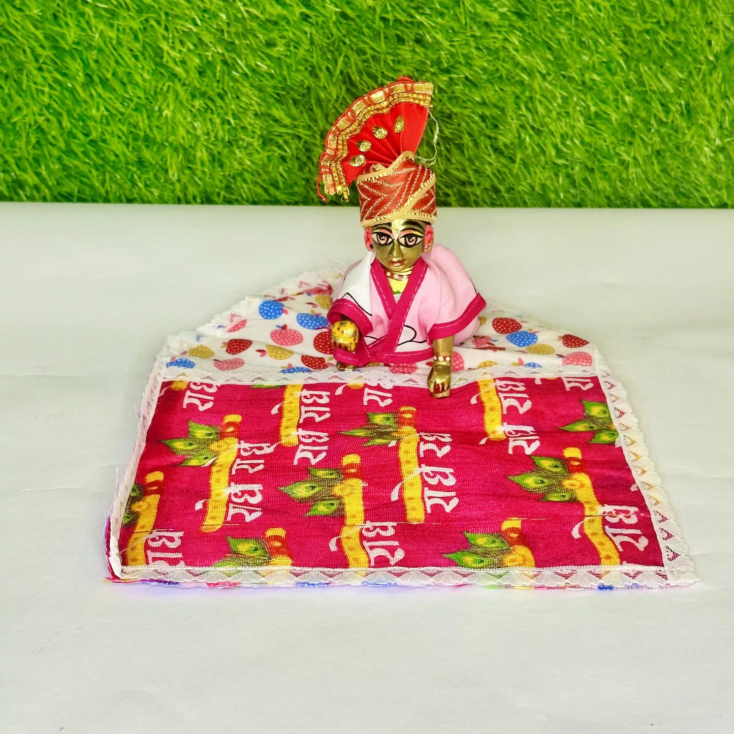 Laddu Gopal ji sitting on a Traditional Cotton Printed Laddu Gopal Bedding Set with Red Radhe Radhe Blanket & Strawberry color Base.